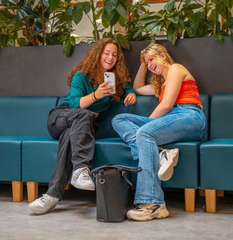 Twee mbo-studenten zitten op een bank en kijken op hun mobiel