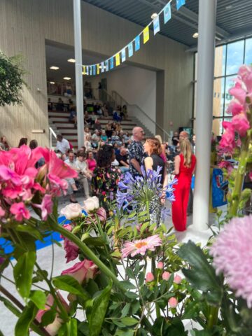 Docenten en volle zaal achter bloemen bij diplomering